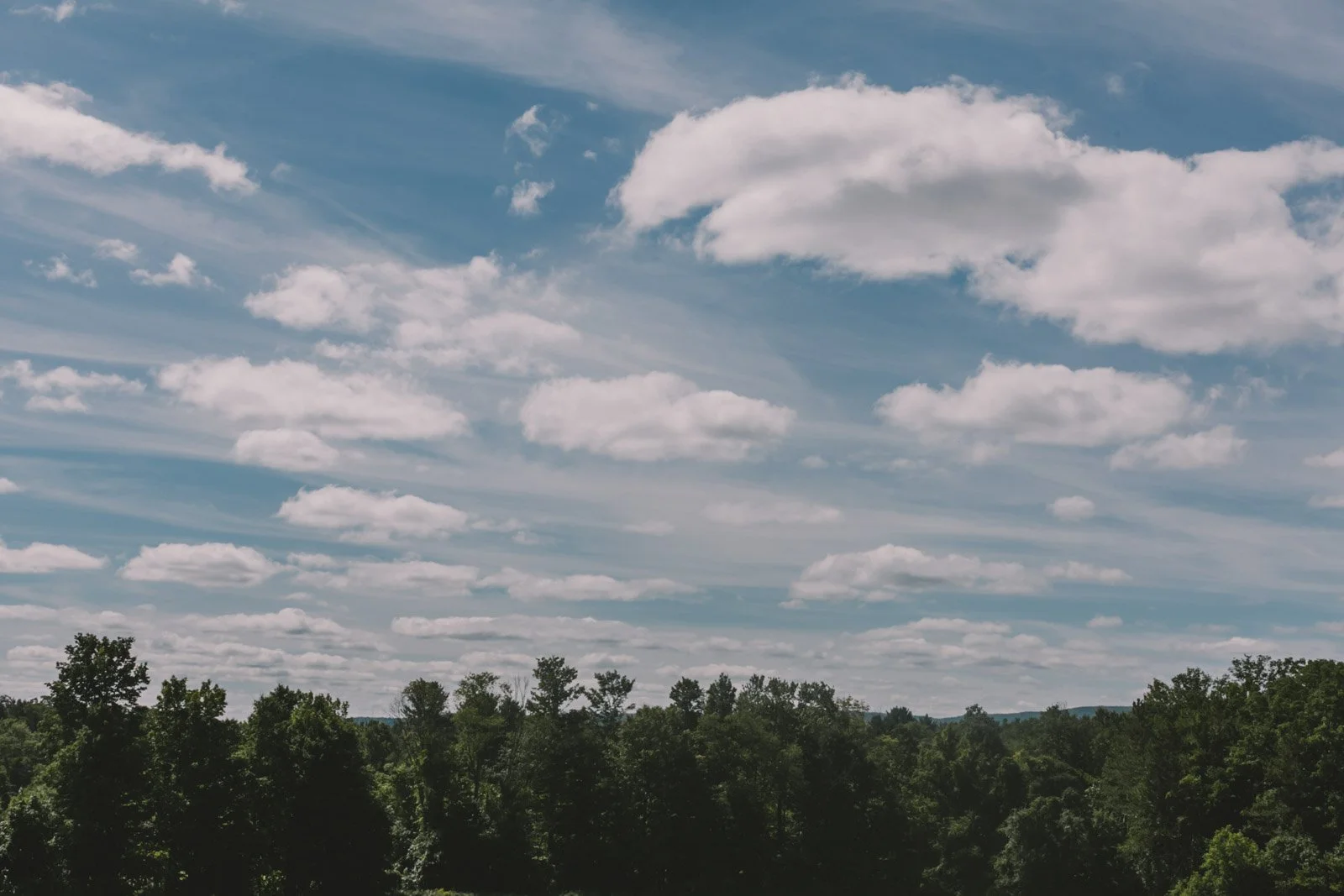 Blue sky with scattered clouds above a forested landscape.