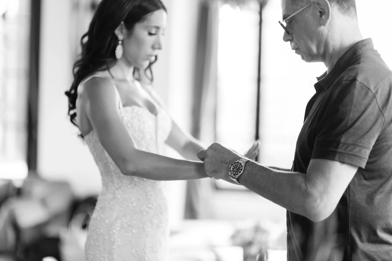 A woman in a wedding dress holding hands with a man in a casual shirt, who is adjusting or holding her hand.