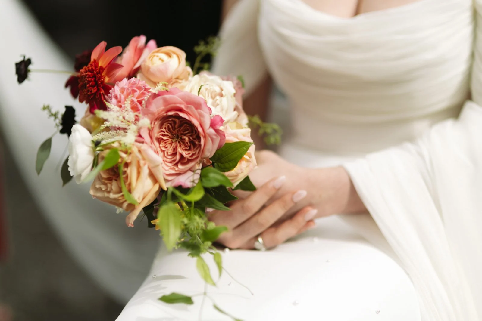 A person in a white dress holding a bouquet of pink and white flowers.