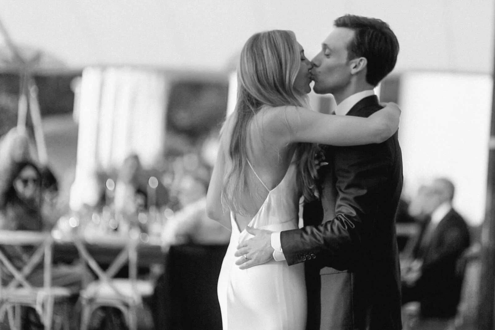 A black and white photo of a bride and groom sharing a kiss during their wedding reception.