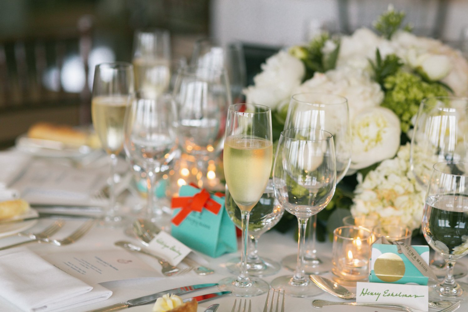 A table set for a celebration with champagne glasses, wine glasses, a floral centerpiece with white and green flowers, candles, and place cards.