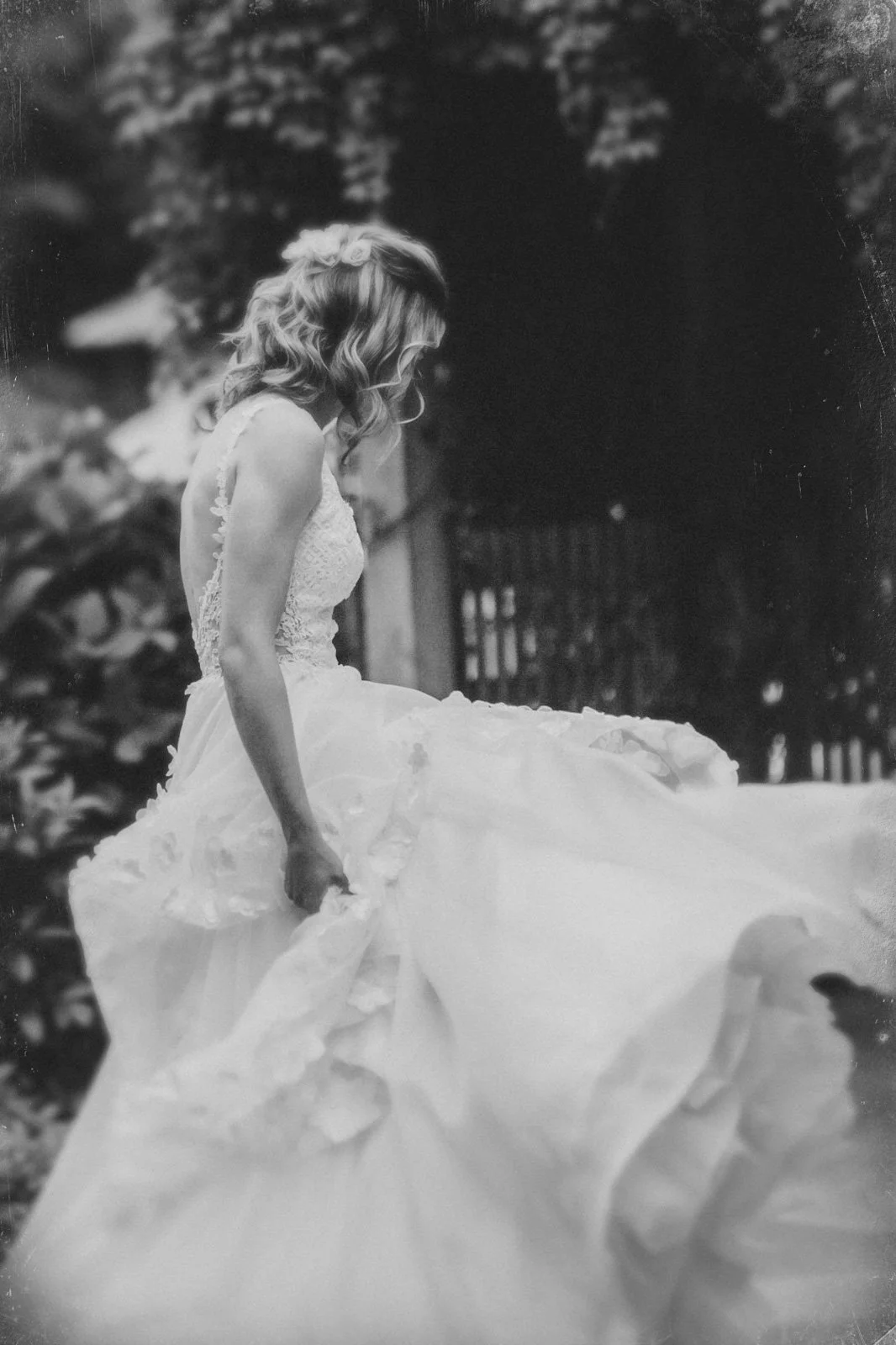 A bride in a wedding dress holding up her gown, sitting outdoors near trees with a blurred background in Southampton.