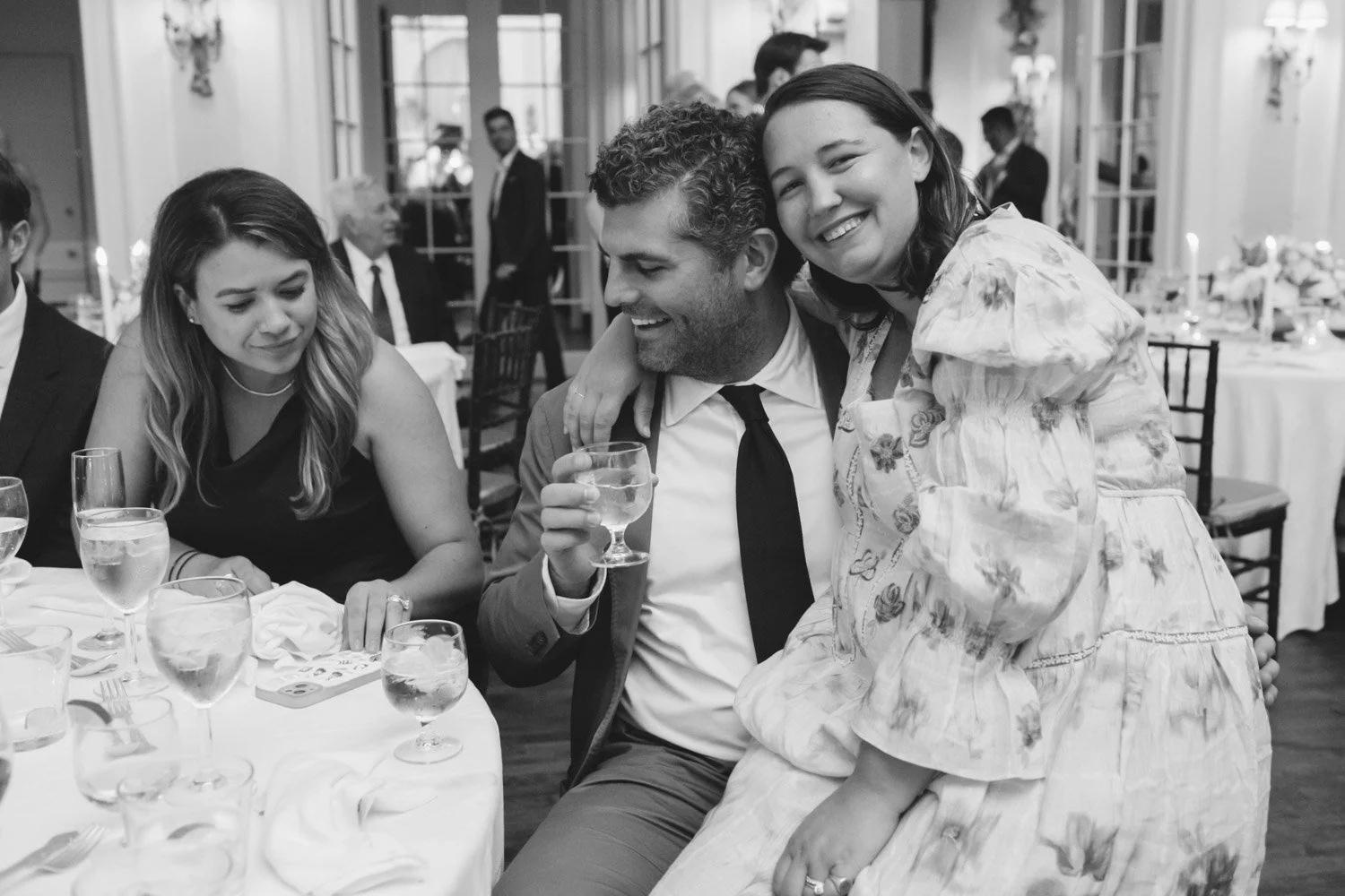 People celebrating at a formal event, with a woman sitting at the table, a man holding a drink, and a girl on his lap smiling.