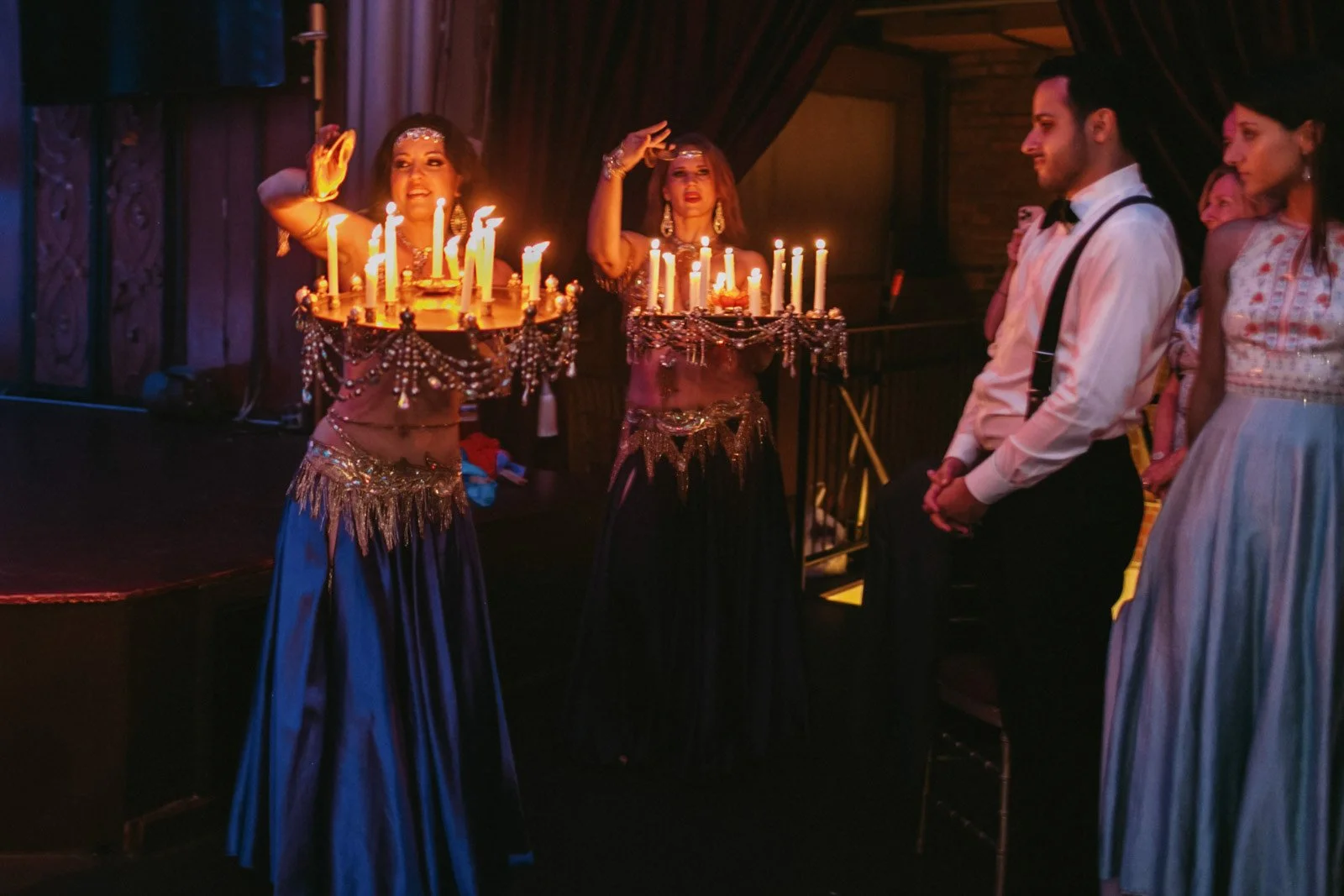 People celebrating birthday with candles and cake in a dimly lit room, some wearing formal or festive attire.