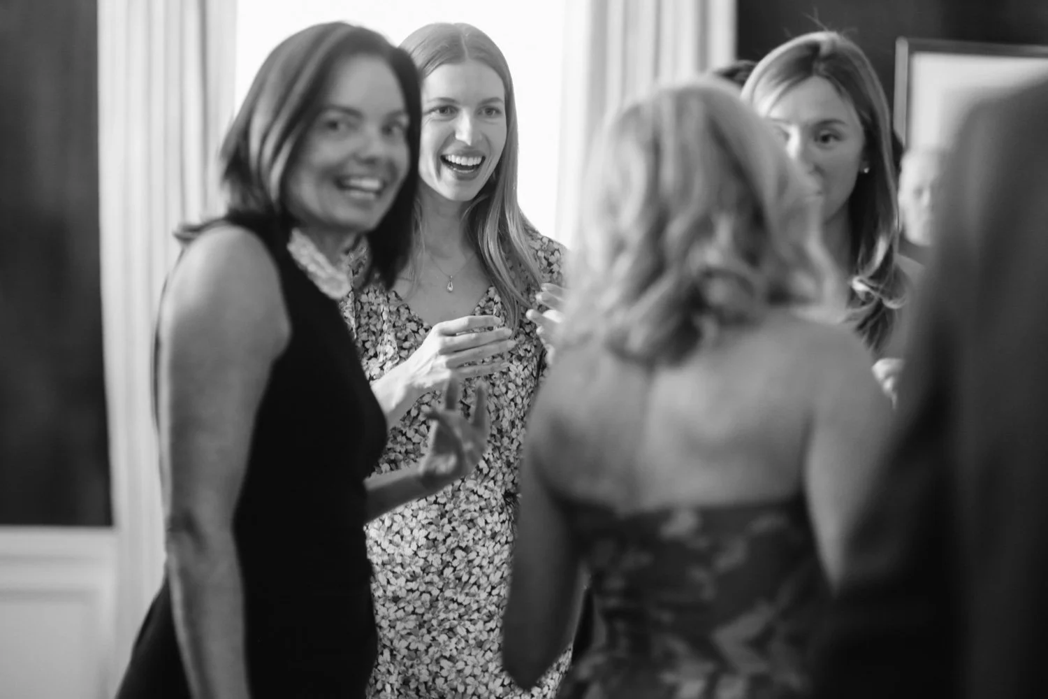 Four women in conversation, smiling and laughing, at an indoor social gathering.