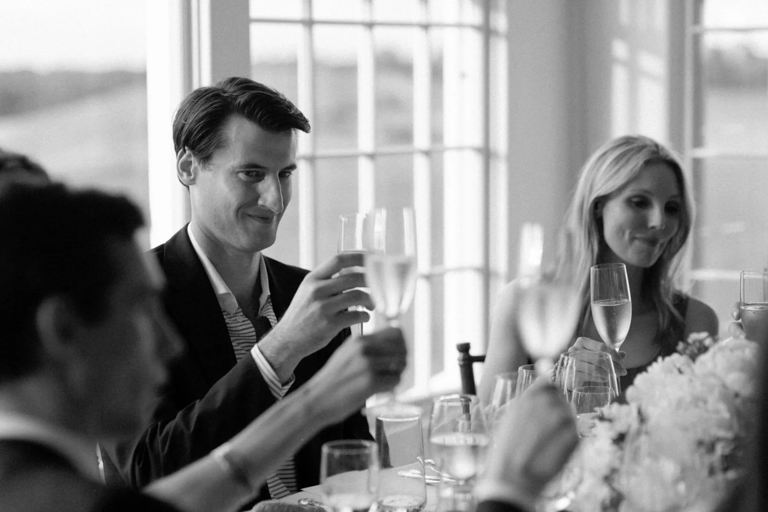 People celebrating with glasses of champagne at a dinner gathering in a bright room.
