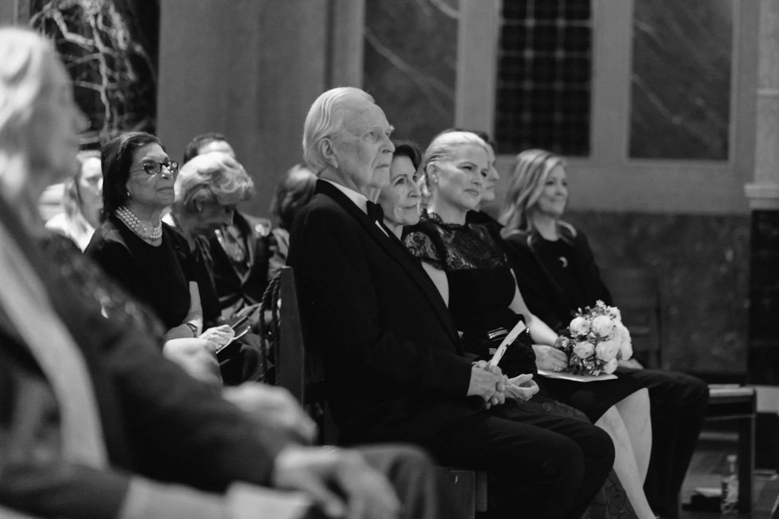 Black and white photo of elderly people sitting in a church or formal event attending a ceremony or service.