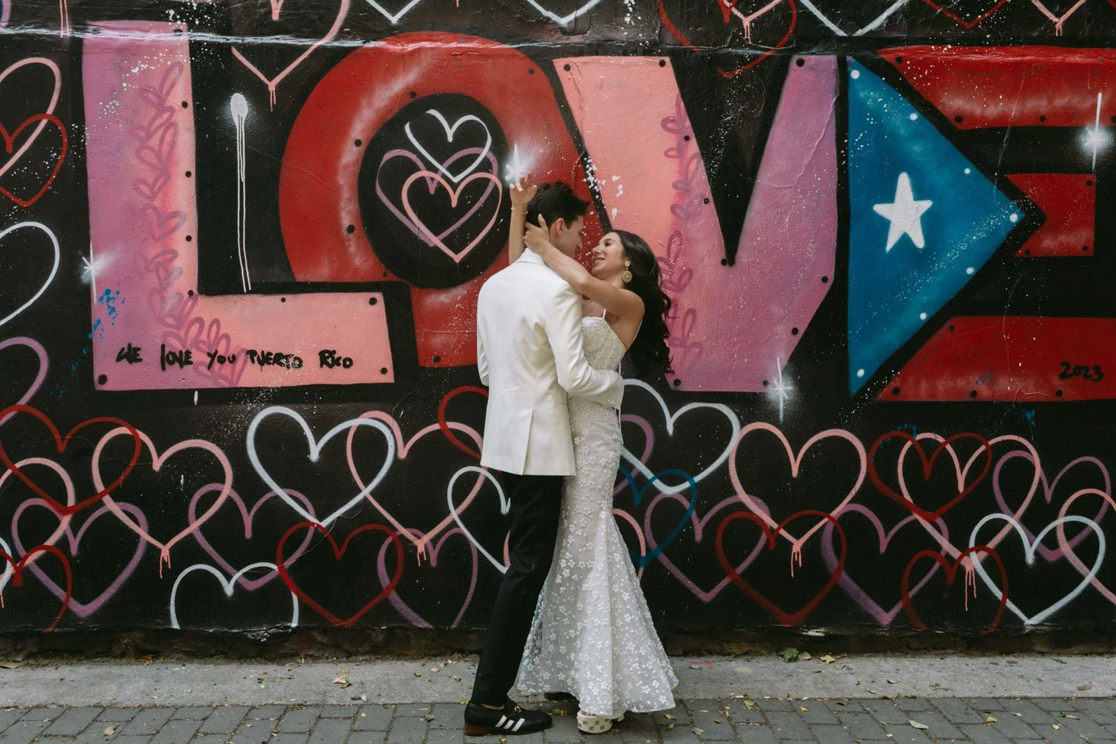 A couple dancing in front of a colorful graffiti mural with hearts and the word "LOVE" and a message "We love you Puerto Rico".