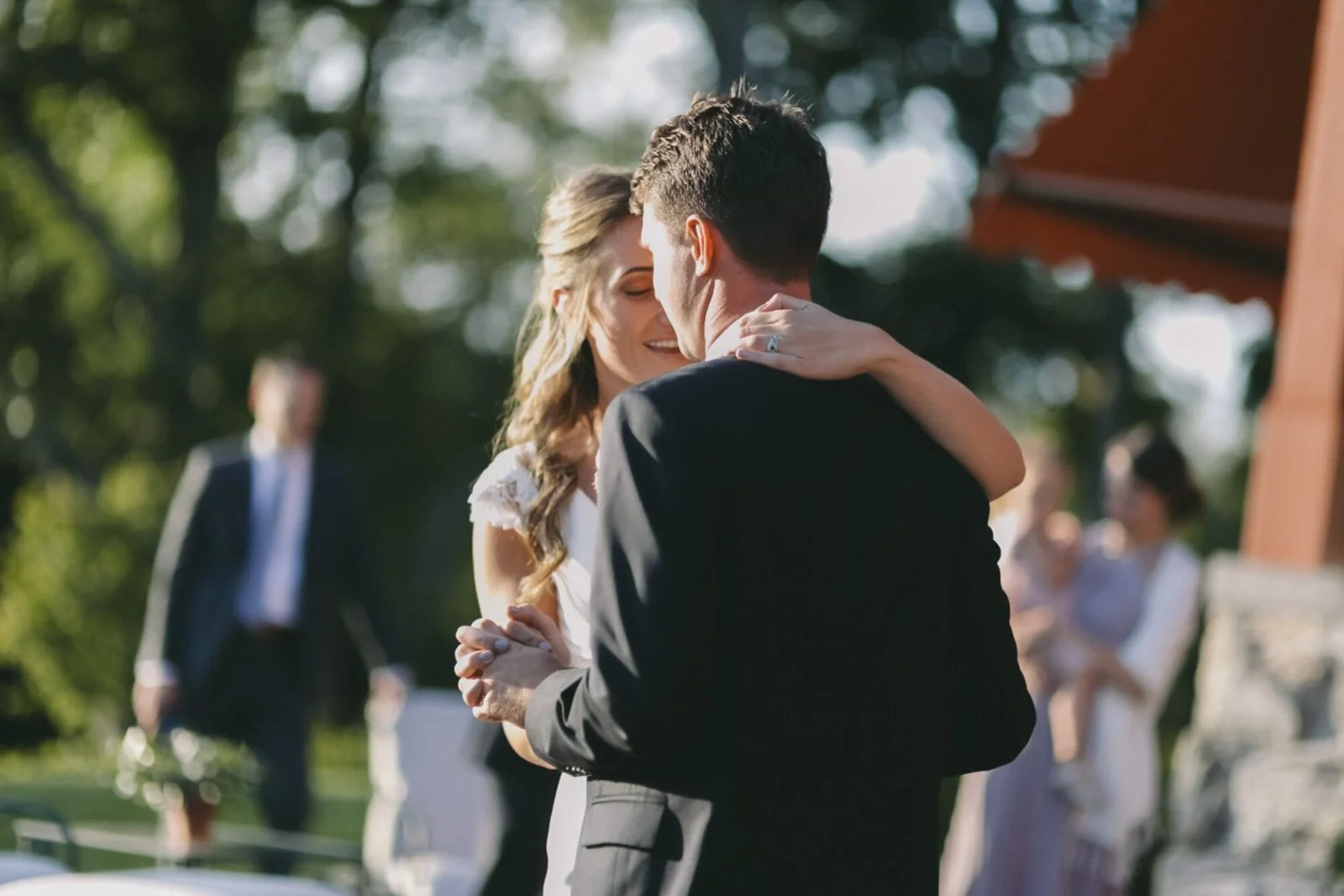 A newlywed couple sharing a dance outdoors during their wedding reception, with guests in the background.