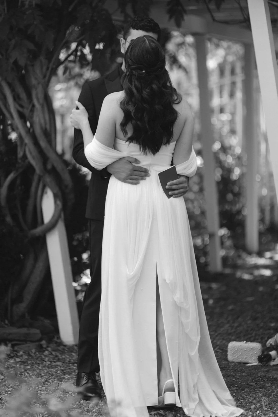 A couple kissing in wedding attire outdoors, black and white photograph.