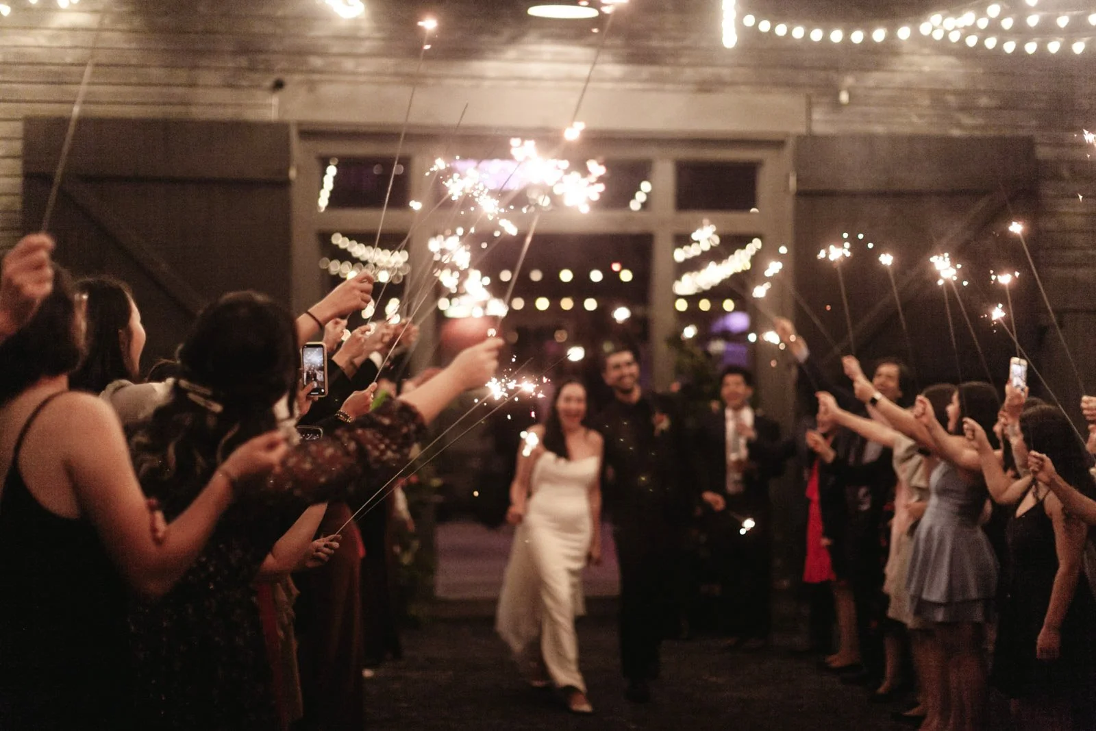 A wedding reception with a bride and groom walking through a tunnel of guests holding sparklers.