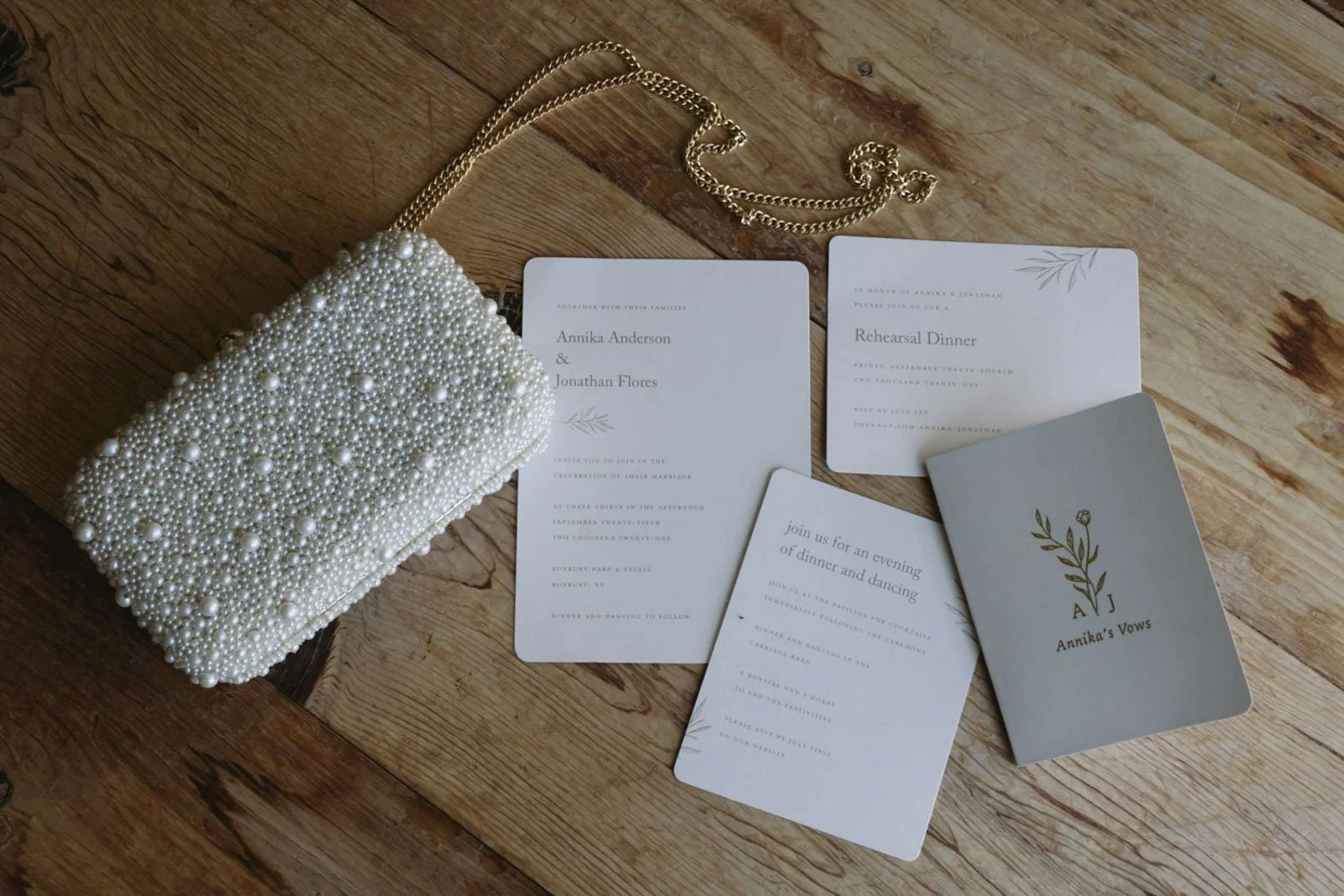 A pearl-embellished clutch, a gold chain, and wedding or event invitations on a wooden surface.