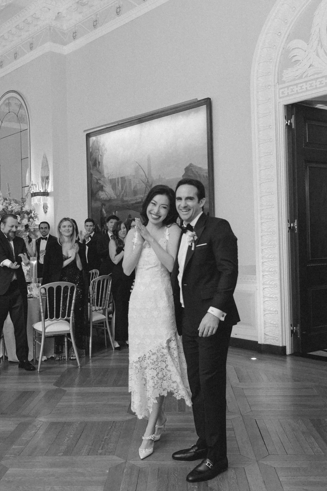 A newlywed couple dancing at a wedding reception with guests watching in a decorated ballroom.