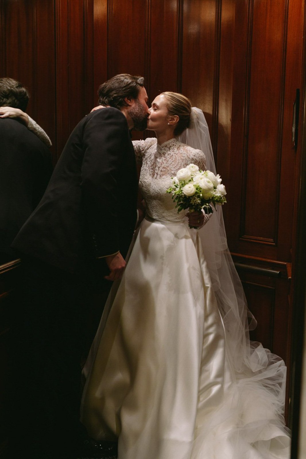 A bride and groom kiss during their wedding ceremony in front of a wooden-paneled wall.