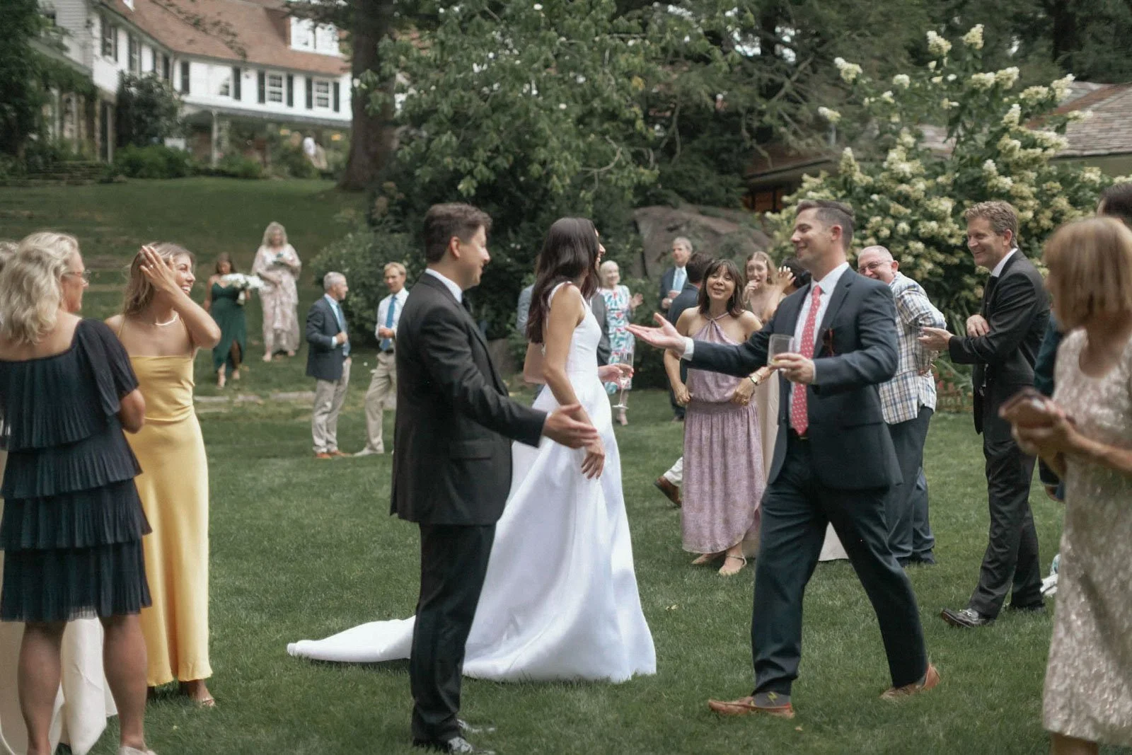 People at a wedding reception outdoors on a lawn, with the bride and groom in the center, socializing and celebrating.