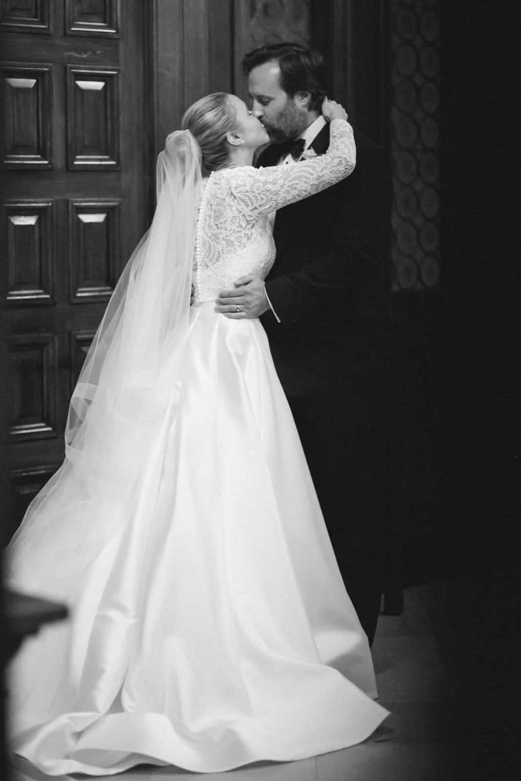 A bride and groom sharing a kiss during their wedding ceremony in a wood-paneled room.
