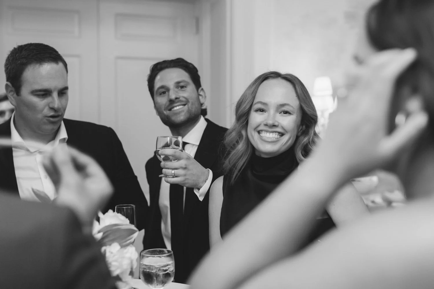 Group of people at a social gathering, smiling and holding drinks, in a formal setting.