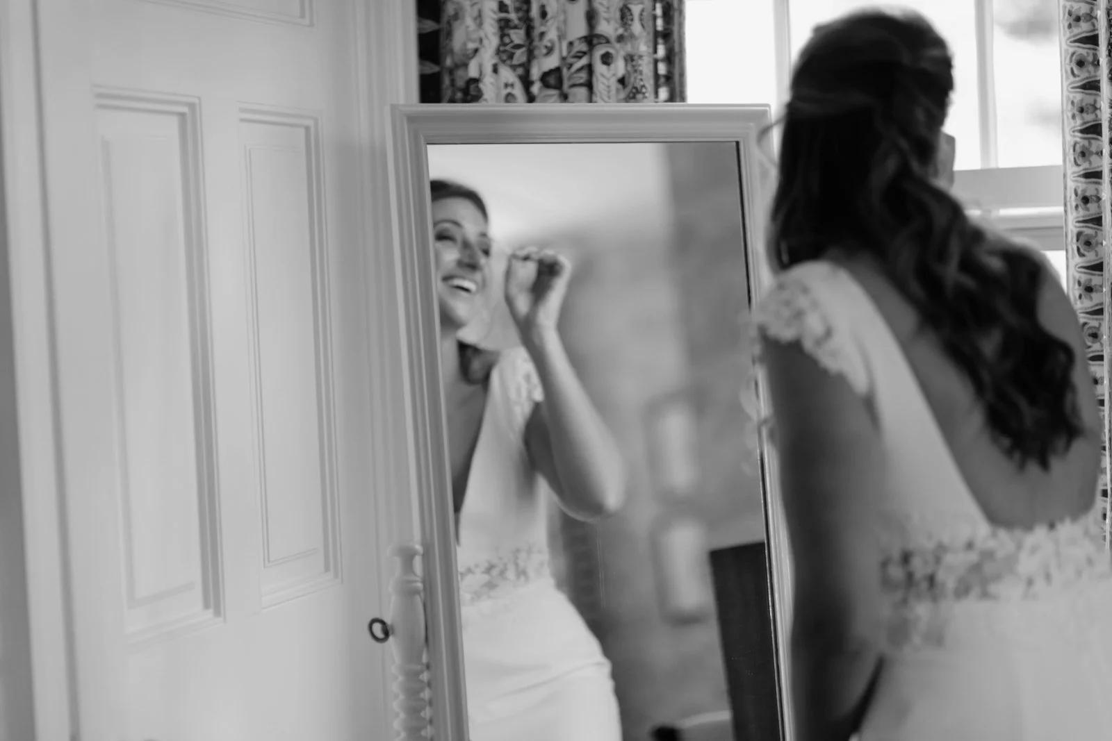 A woman in a wedding dress applies makeup while looking at her reflection in a mirror.