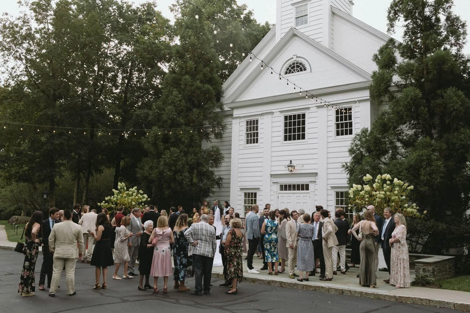 Guests gather outside Stanwich Church in Greenwich, CT, for a wedding celebration with string lights and floral arrangements.