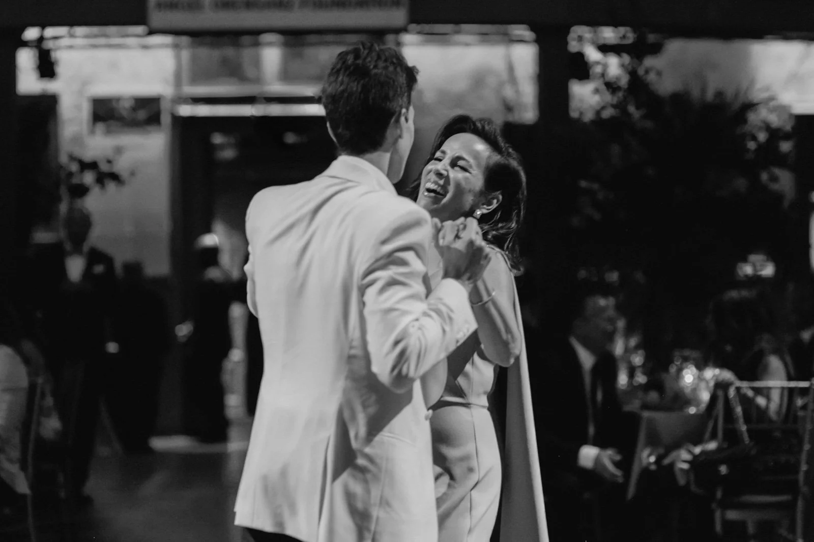 Black and white photo of a joyful couple dancing at their wedding reception, surrounded by seated guests.