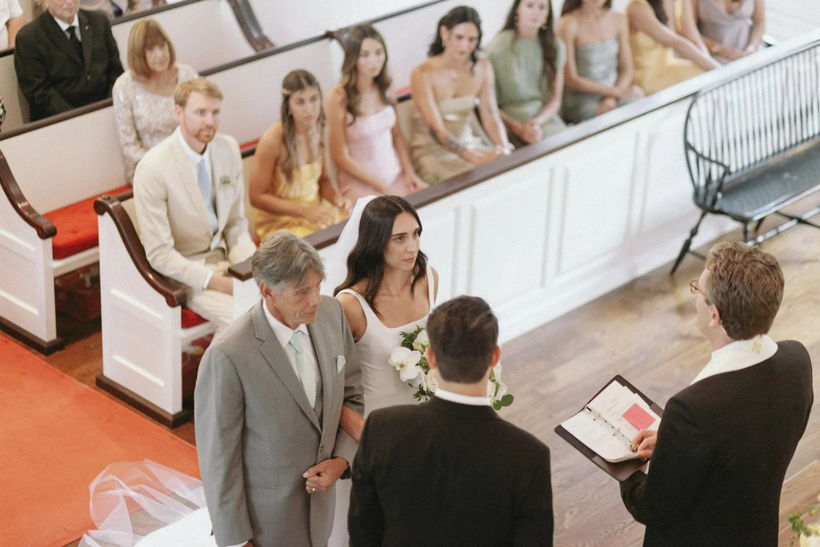 A wedding ceremony inside a church, with the bride and groom facing officiants, and guests seated in the pews.