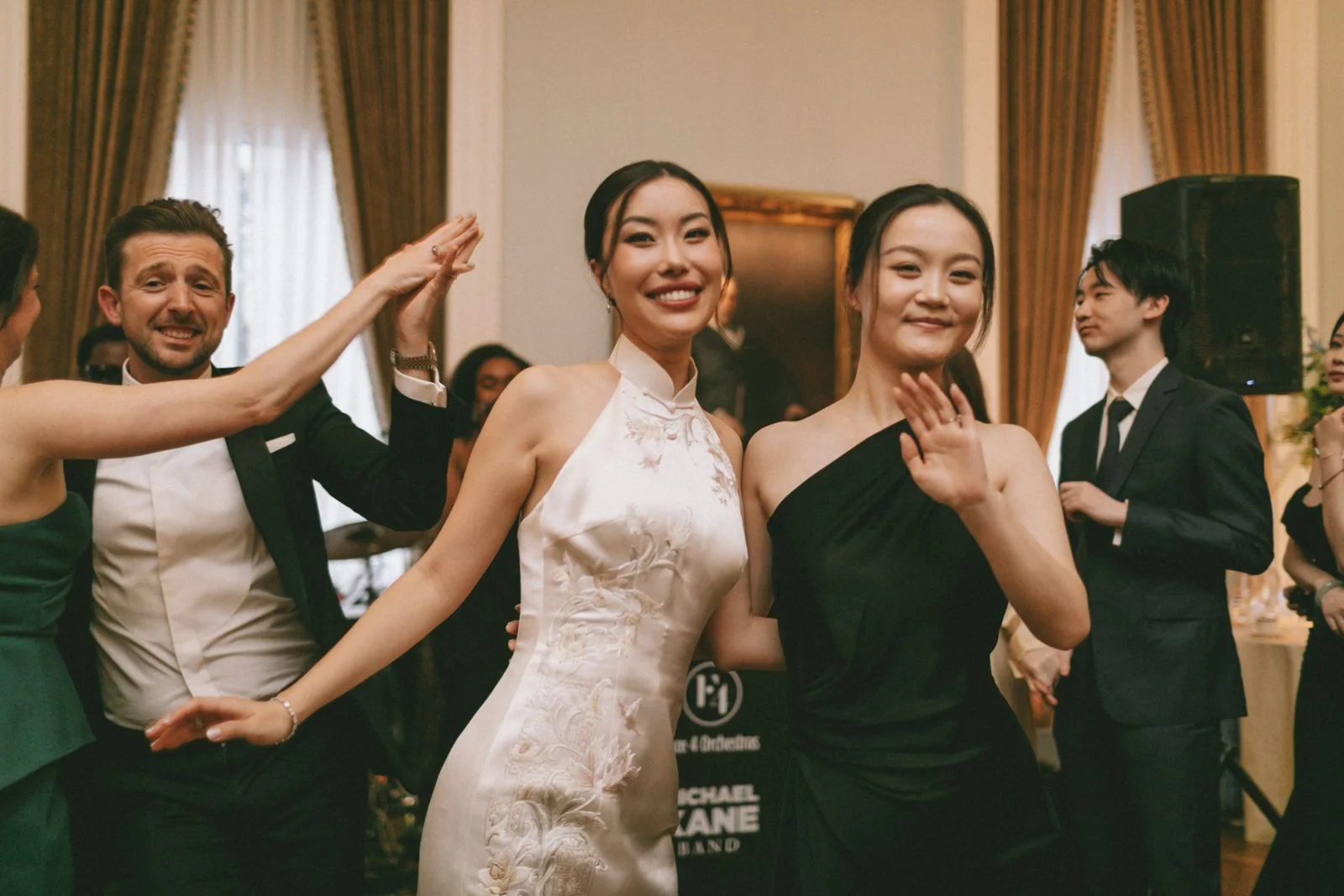 People dancing at an indoor event with elegant decor, including gold curtains and framed artwork.