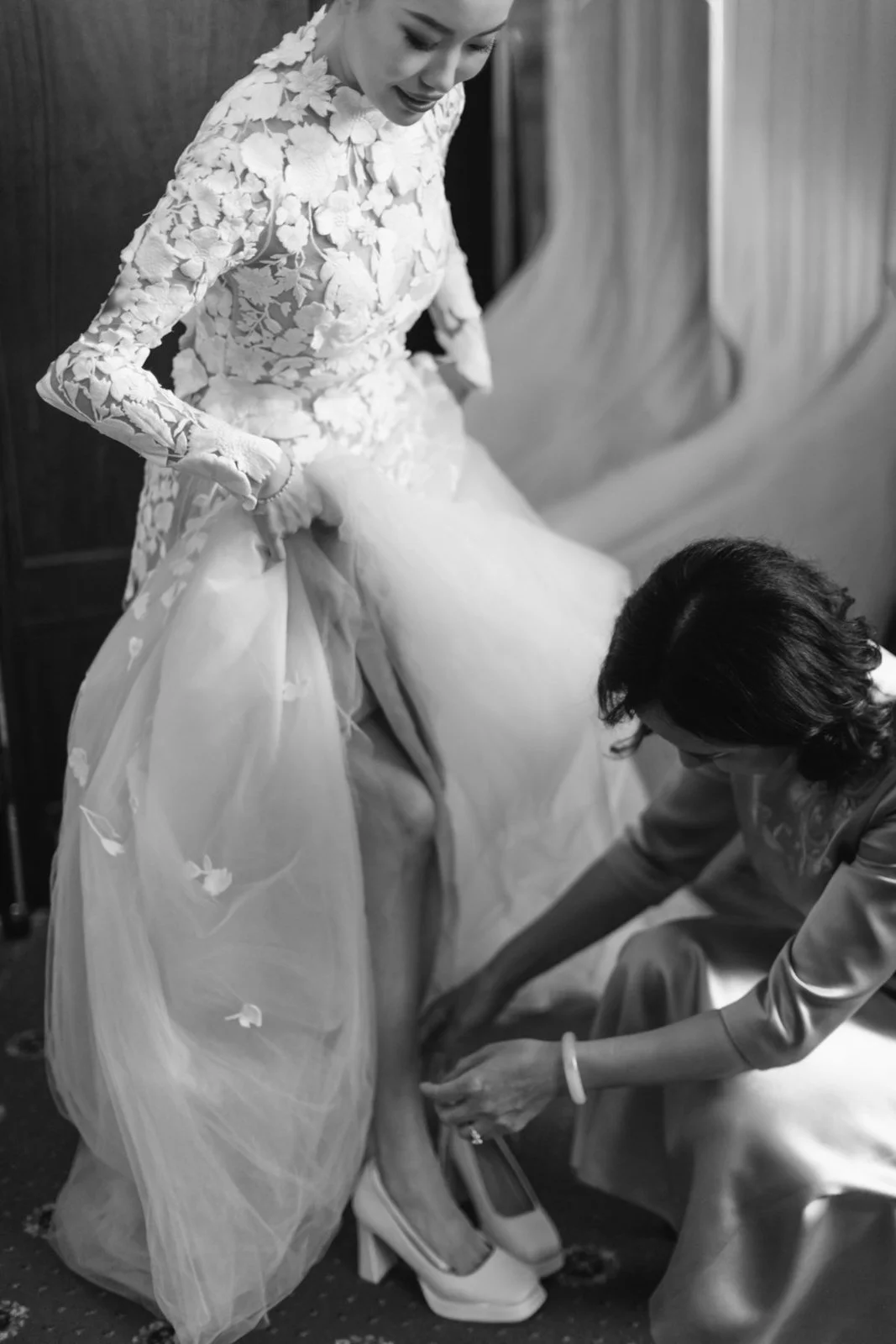 A woman in a wedding dress having her shoe fitted by another woman.