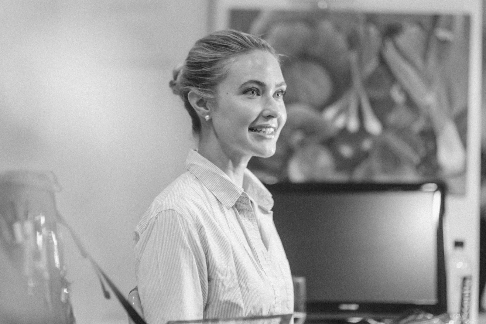 Black and white photo of a woman with her hair styled in an updo, smiling and sitting indoors.