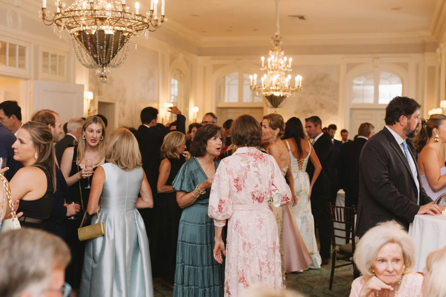People socializing and conversing at a formal event or party in an elegant ballroom with chandeliers.