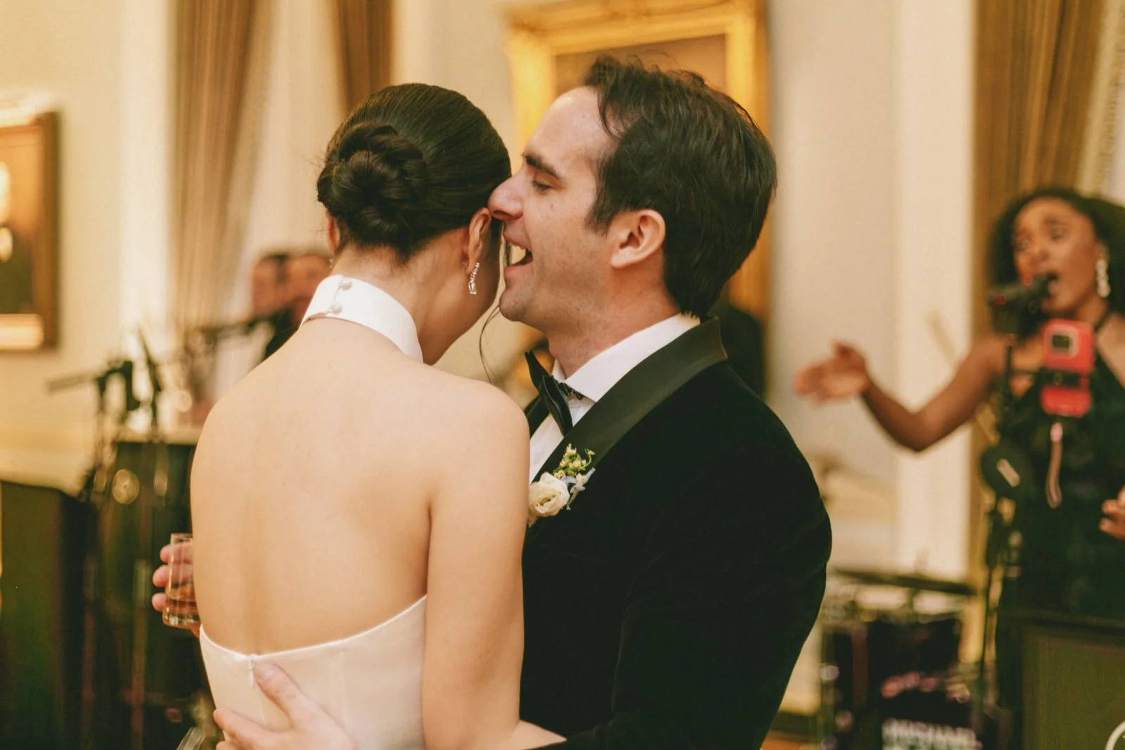 A groom and bride dancing closely at a wedding reception, with a musician and singer playing in the background.