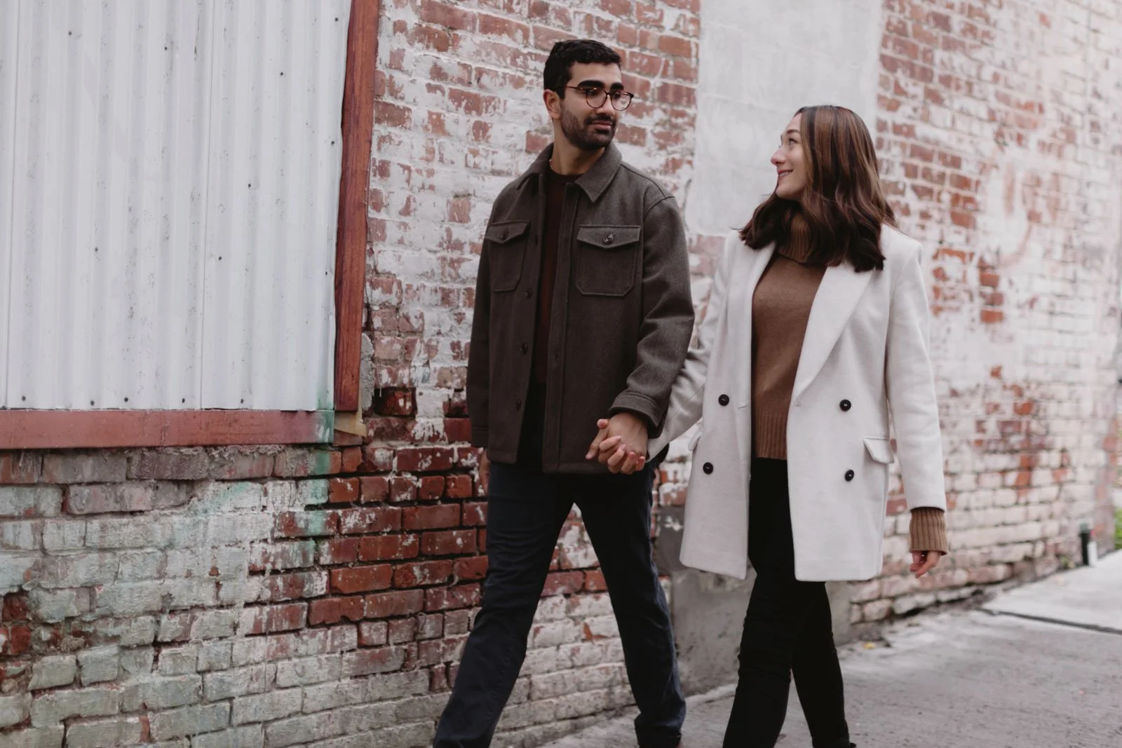 A couple walking hand in hand along a brick wall in an urban setting.
