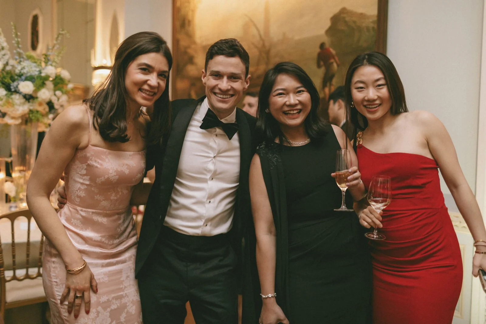 Group of four people smiling and dressed in formal attire at a celebration, holding wine glasses.
