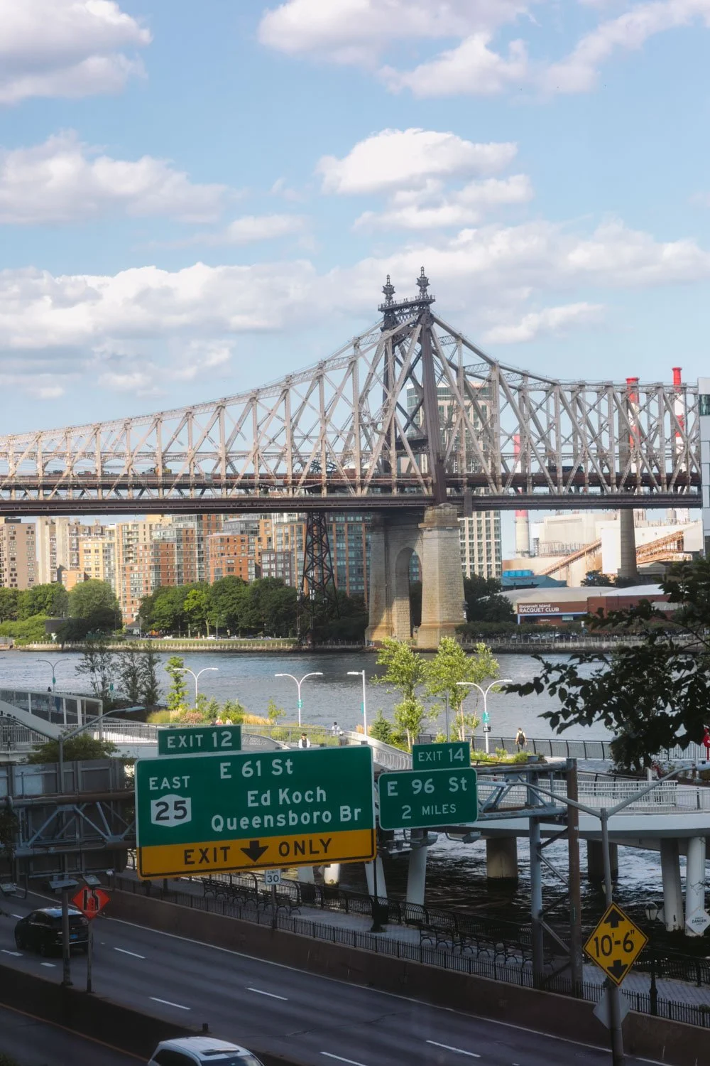 View of a bridge over the water with city buildings in the background and highway signs indicating exits and streets below.