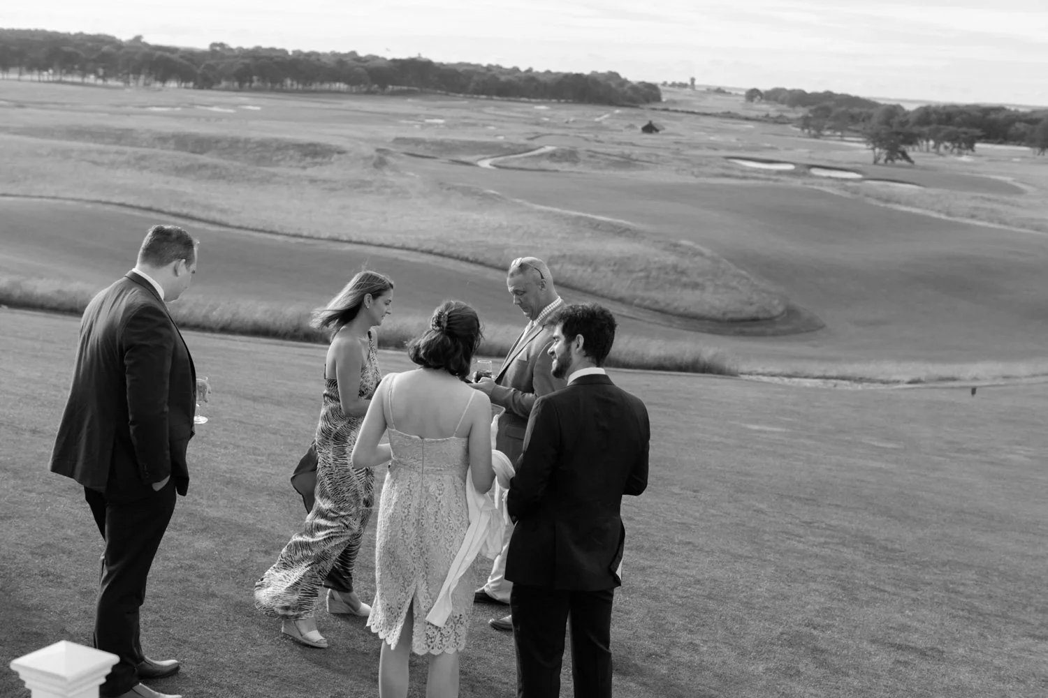 Group of people in formal attire standing on a golf course during daytime.