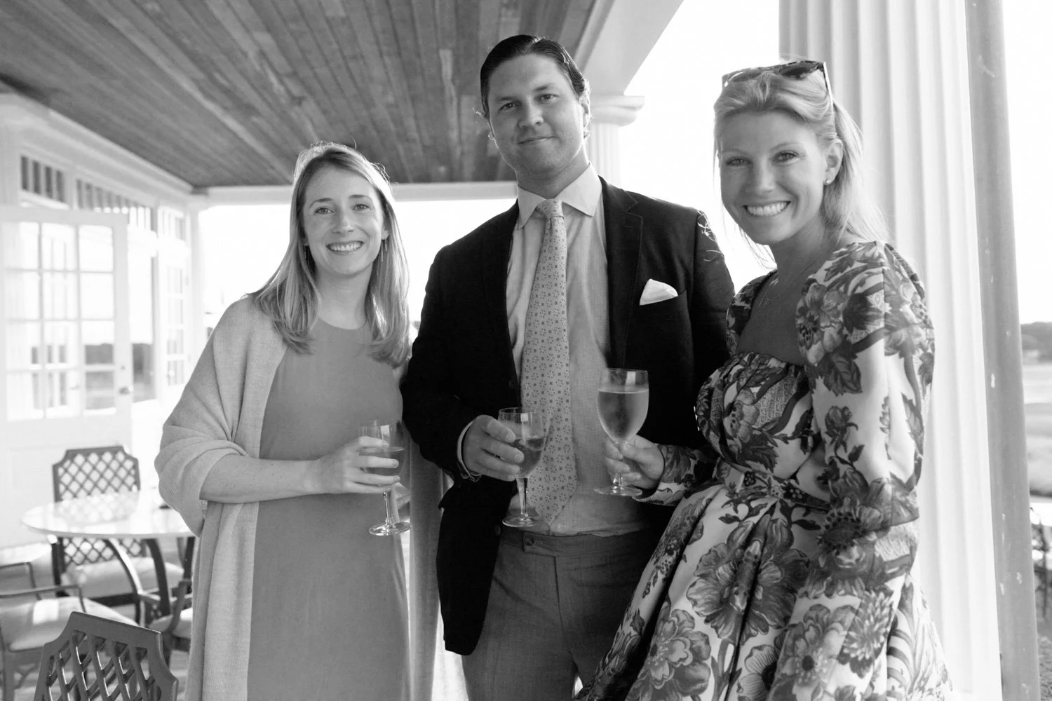 Three women and one man smiling and holding champagne glasses at an outdoor gathering or celebration.