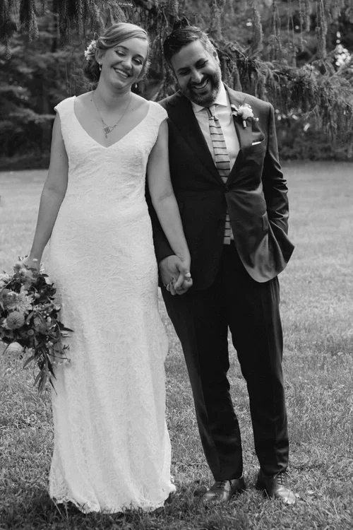 A bride and groom walking hand in hand outdoors on a grassy area, smiling and holding hands.