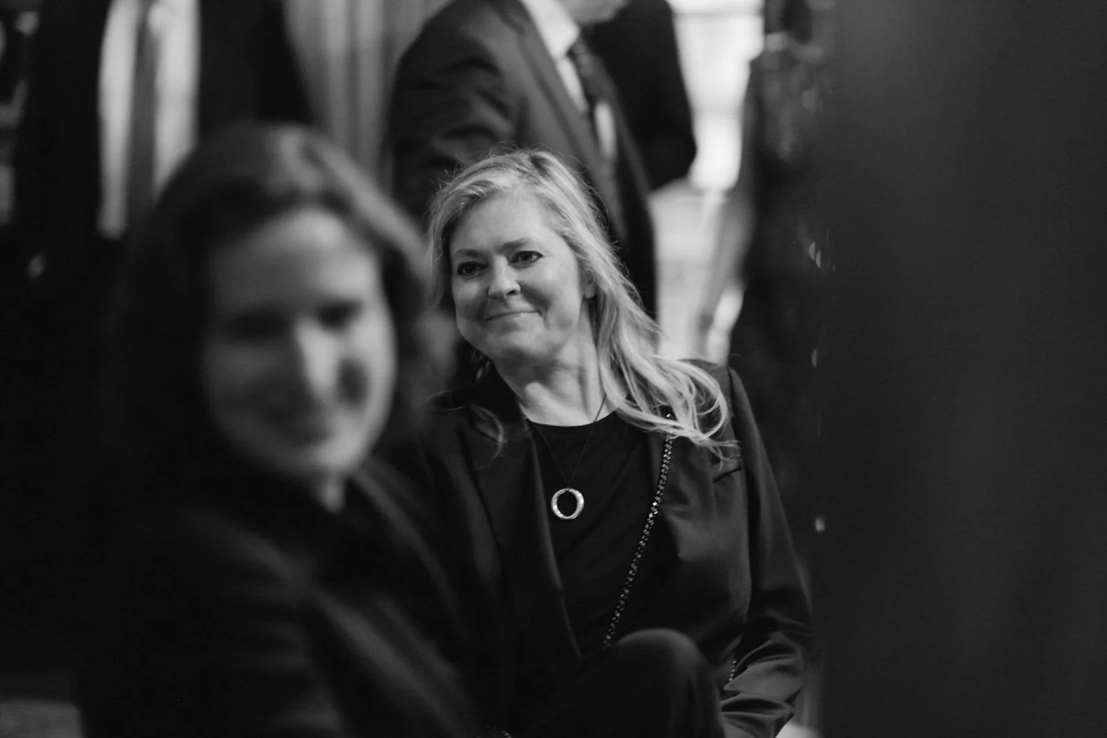 Two women sitting in a public venue, with one woman in focus smiling and the other woman blurred in the foreground.