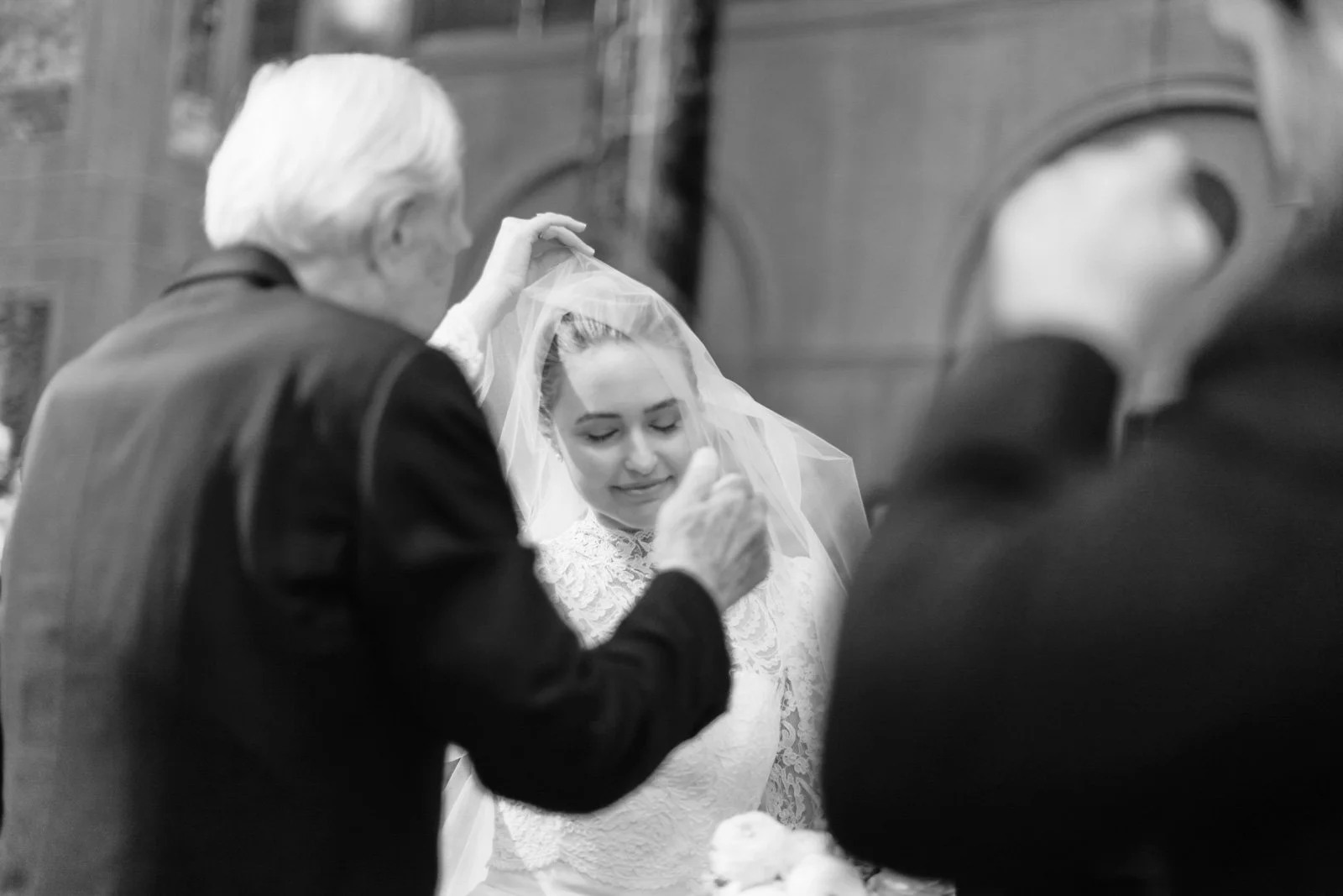 An elderly man adjusting a veil on a bride during a wedding ceremony in a church.