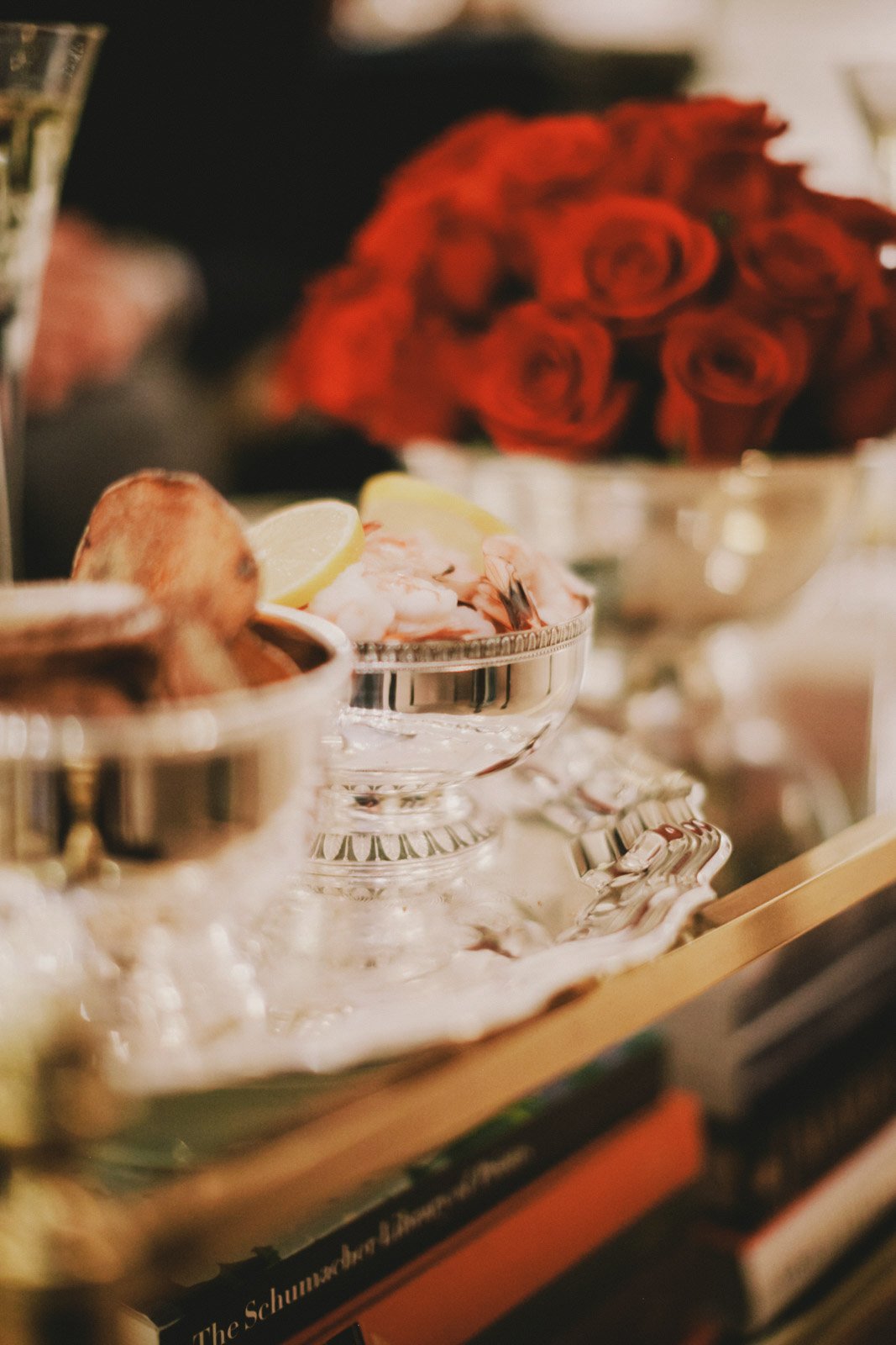 A display of seafood on silver trays with lemon wedges, with a bouquet of red roses in the background.