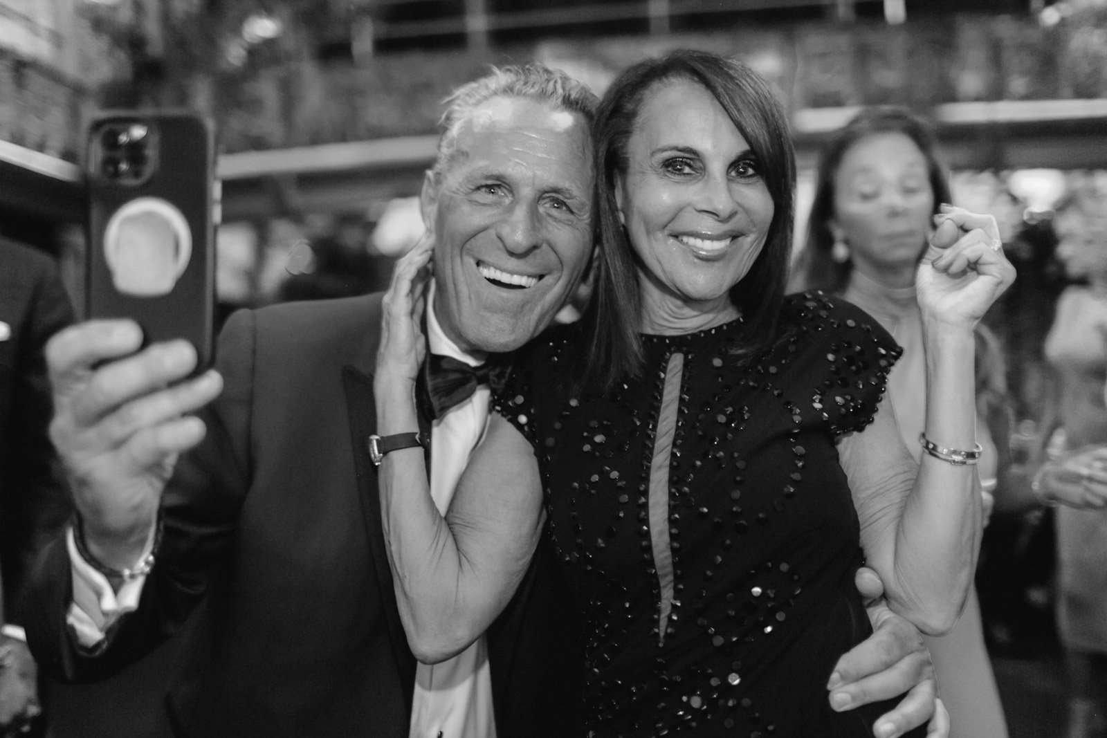 A man and woman taking a selfie at an event, smiling and dressed formally with the woman in a sparkly dress.
