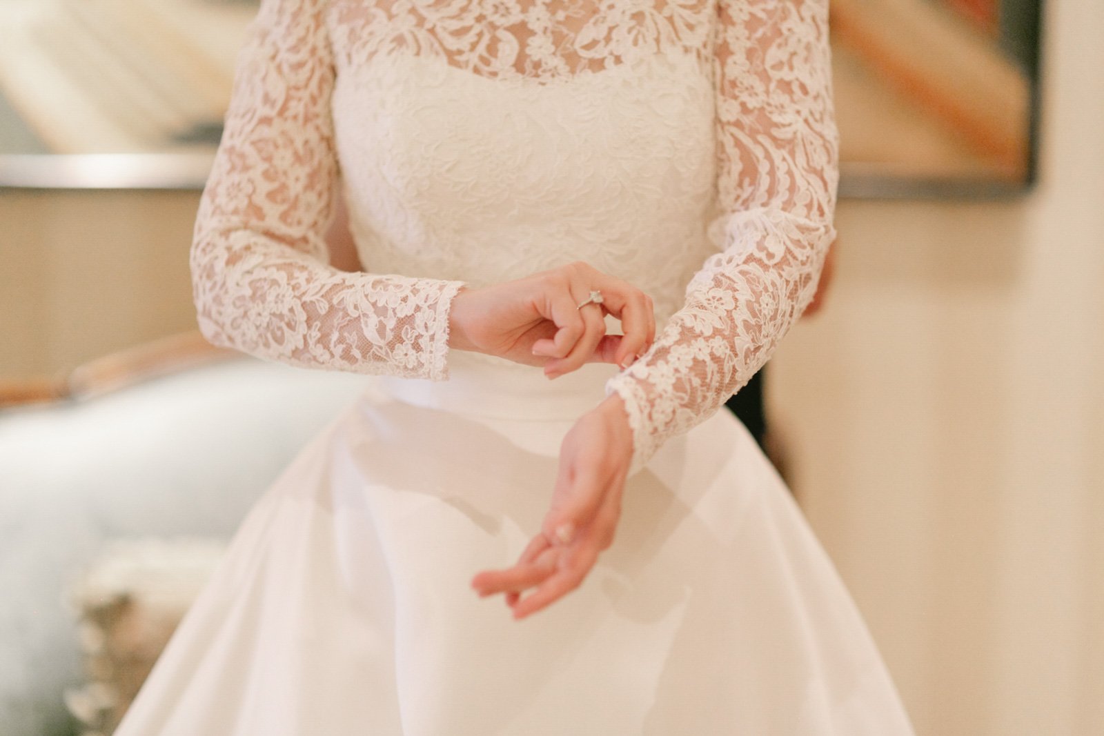 Close-up of a bride wearing a lace wedding dress, adjusting her dress with her hands.