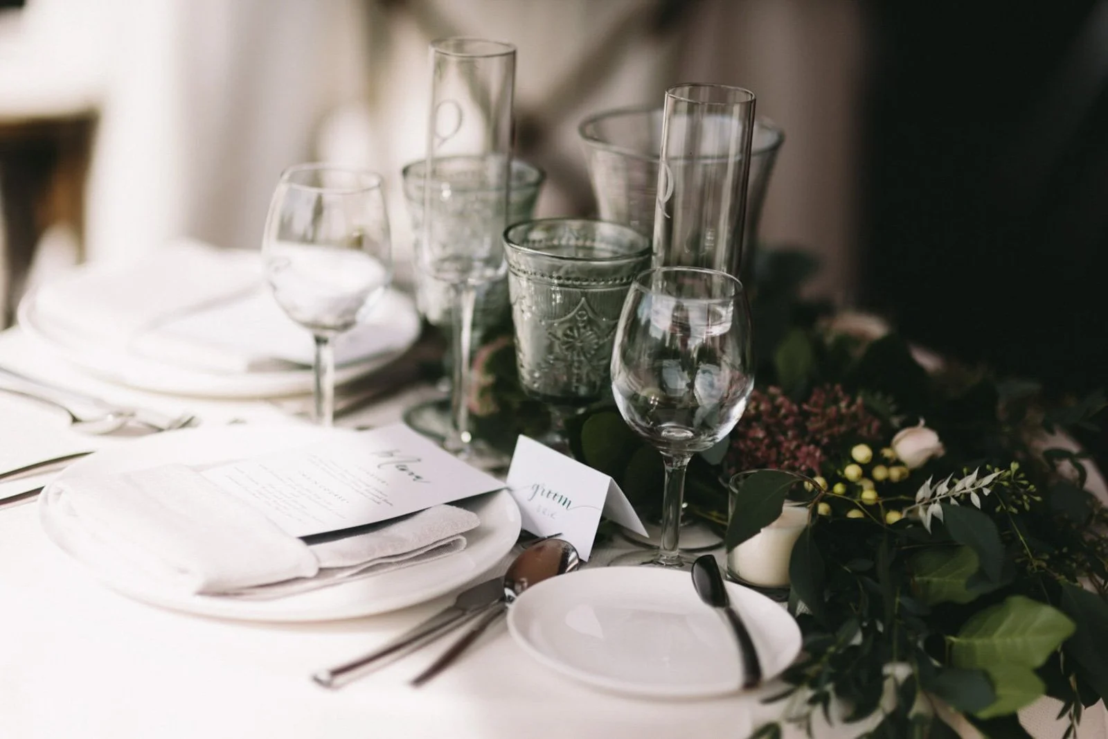 Elegant dining table set with plates, glasses, silverware, a menu, and floral decorations.