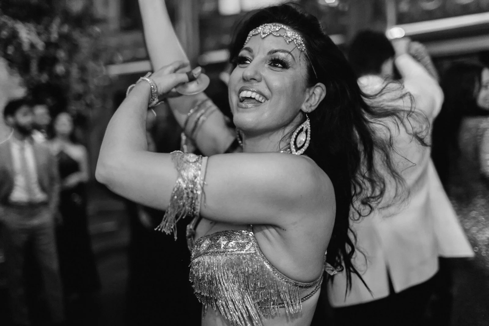 A woman dancing and smiling at a lively event, wearing ornate jewelry and a sparkly outfit.