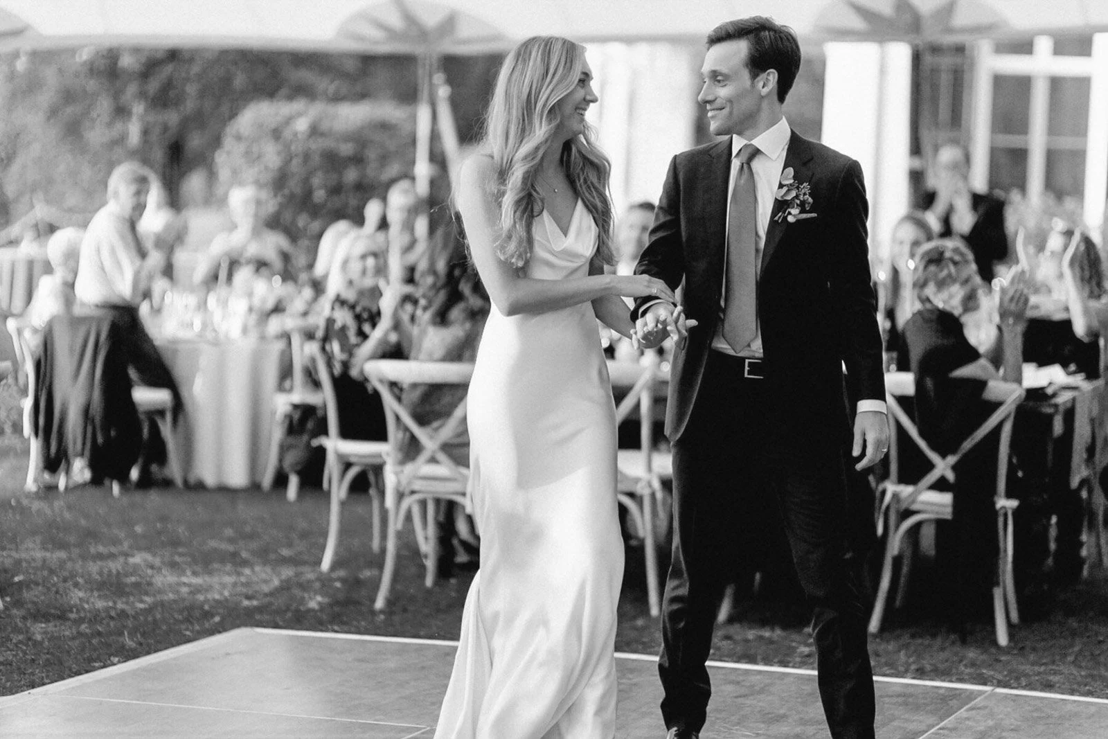 A bride and groom dancing at their wedding reception with guests seated at tables in the background.