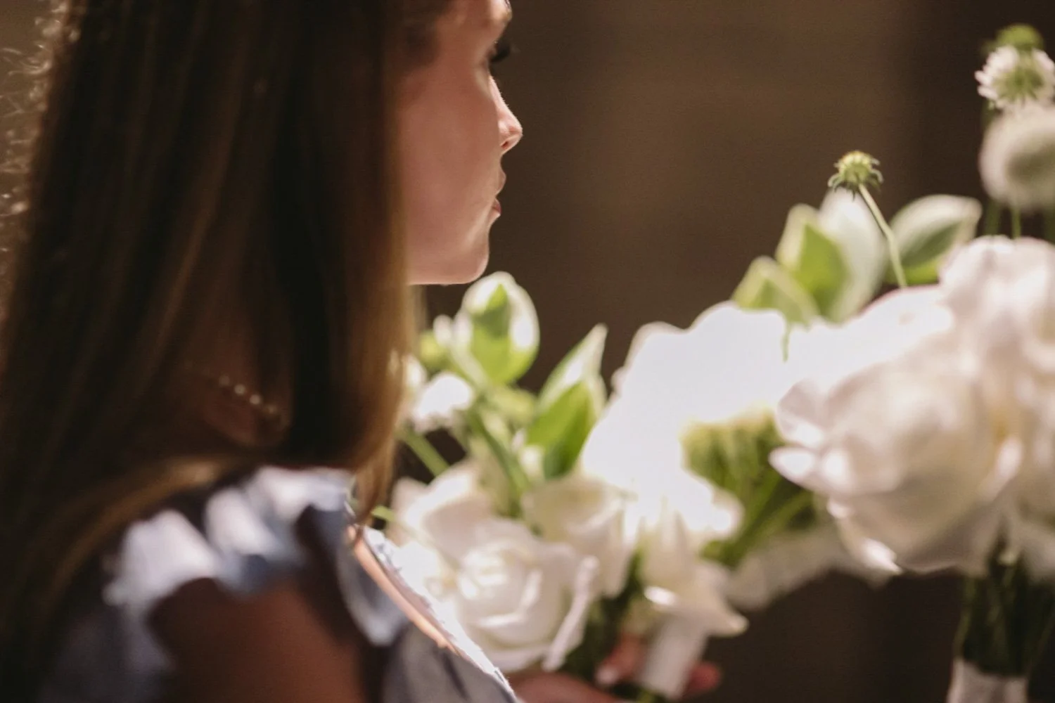 A woman with straight brown hair is holding a bouquet of white flowers.