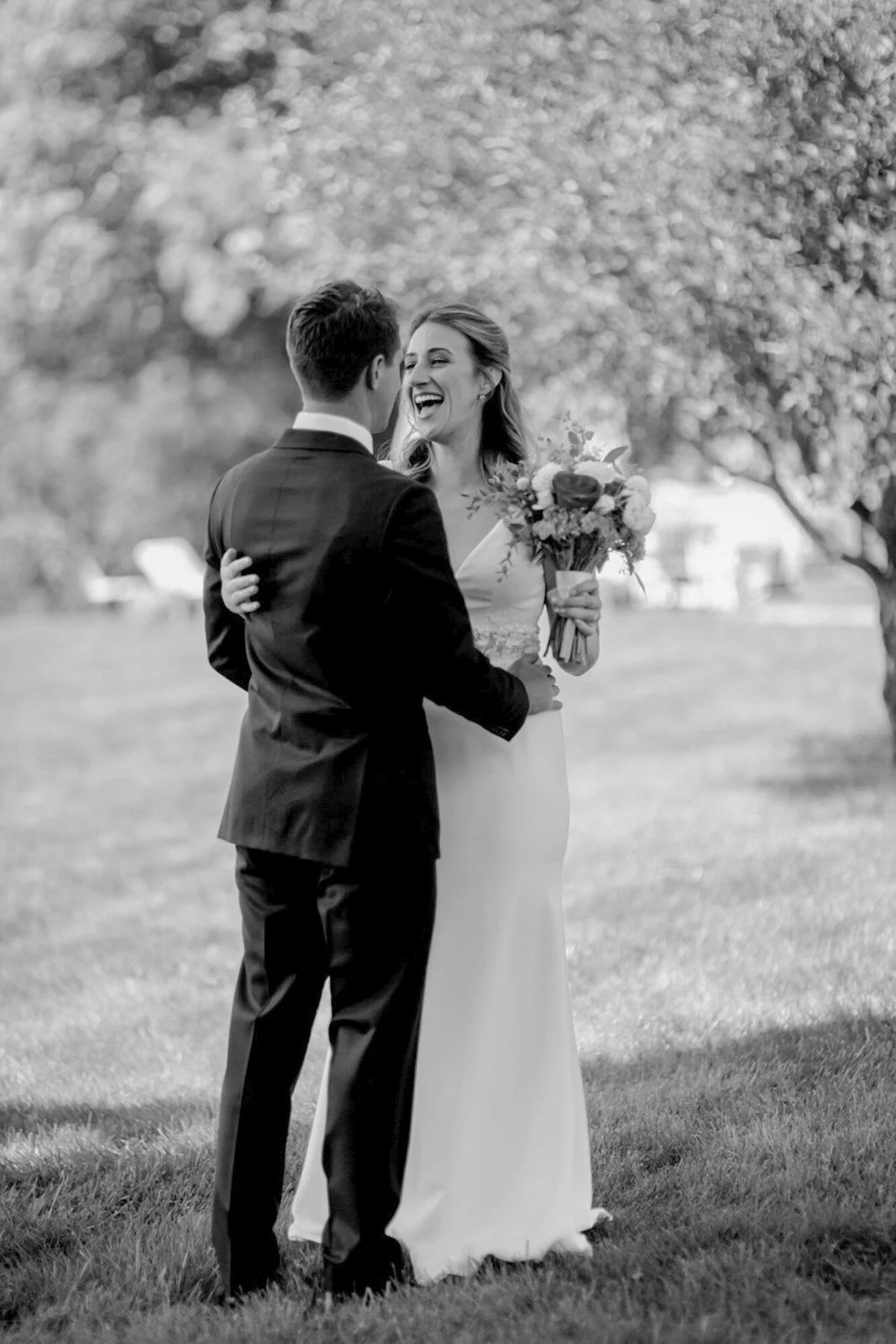 A wedding couple standing outdoors, the bride holding a bouquet of flowers, smiling and looking at each other