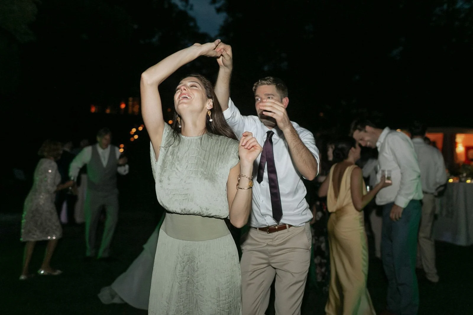 A woman and a man are dancing together at an outdoor evening event, surrounded by other people socializing and enjoying drinks.