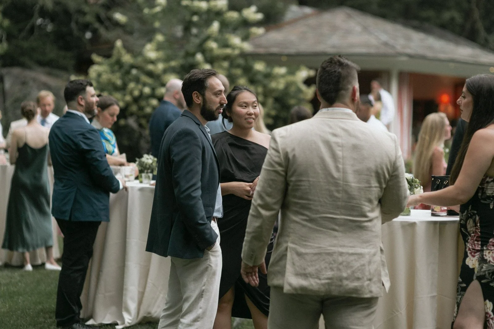 People socializing at an outdoor event, dressed in semi-formal attire, with a buffet table in the background.