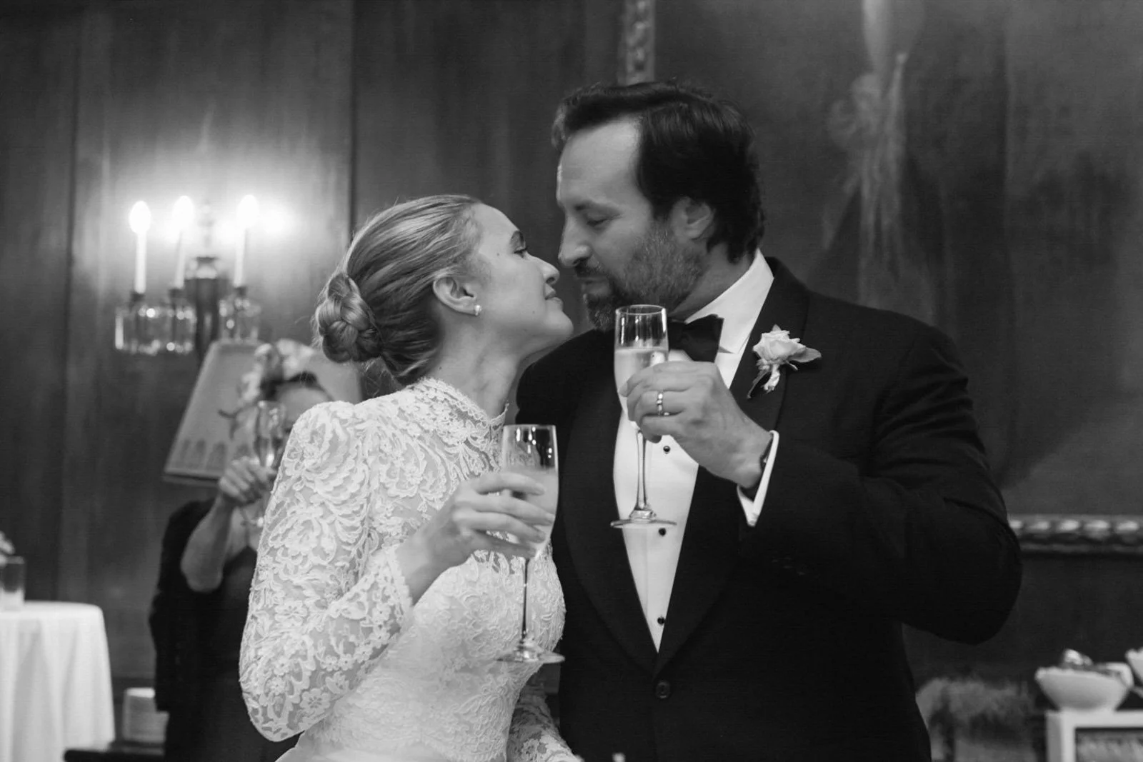 Black and white photo of a wedding reception with a bride and groom sharing a close moment, holding champagne glasses.