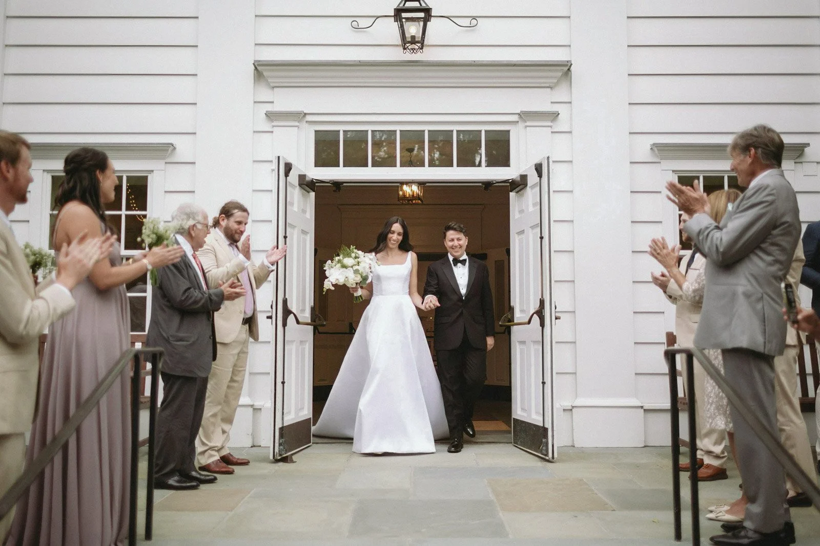 A newlywed couple walking out of Stanwich Church in Greenwich, CT, surrounded by friends and family clapping and celebrating.